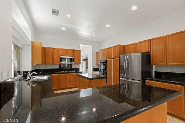 kitchen with a sink, visible vents, appliances with stainless steel finishes, a center island, and dark stone countertops