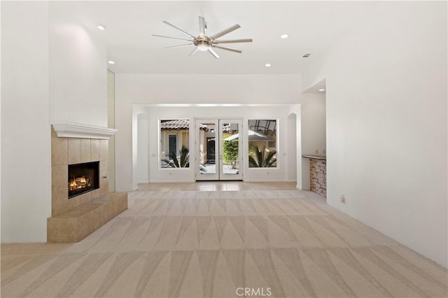 unfurnished living room featuring arched walkways, recessed lighting, light colored carpet, a ceiling fan, and a tile fireplace