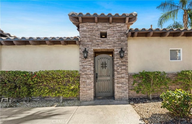 property entrance featuring stone siding, a tile roof, and stucco siding