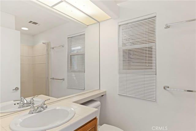 full bathroom with toilet, visible vents, tiled shower, and vanity