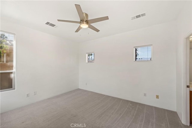 carpeted spare room with a ceiling fan, visible vents, and a wealth of natural light