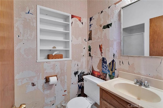 half bathroom featuring built in shelves, tile walls, vanity, and toilet