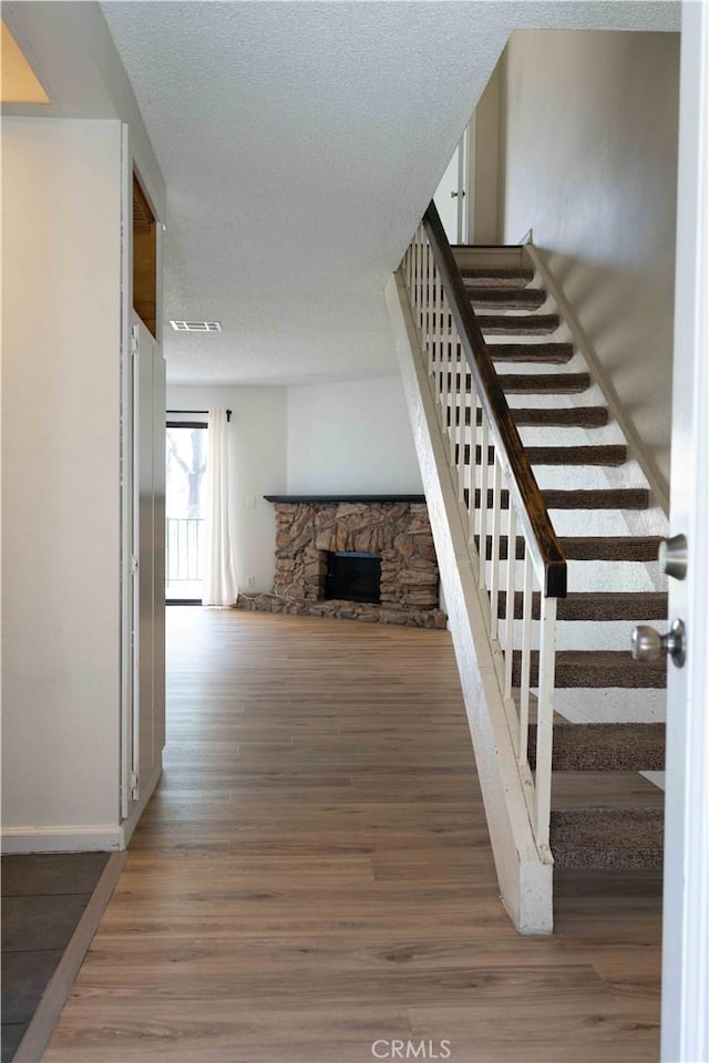 stairs featuring visible vents, a textured ceiling, wood finished floors, a fireplace, and baseboards