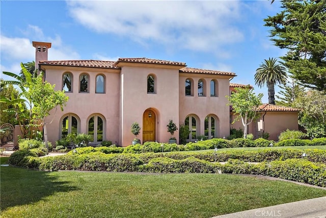 mediterranean / spanish house with a front lawn, a tile roof, and stucco siding