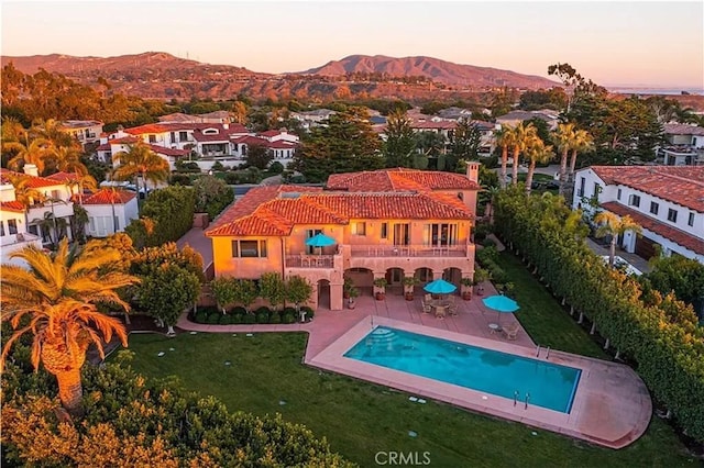 pool at dusk with a yard, a patio, a mountain view, a residential view, and an outdoor pool