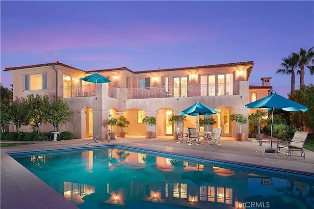 pool at dusk with a patio and an outdoor pool