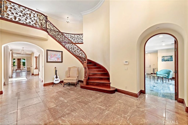 foyer entrance with baseboards, a high ceiling, arched walkways, and ornamental molding