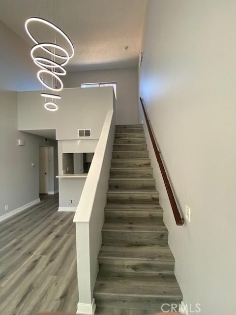 stairs featuring baseboards, wood finished floors, visible vents, and a notable chandelier