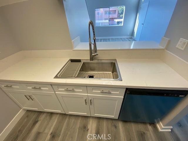 kitchen with light countertops, stainless steel dishwasher, dark wood-type flooring, white cabinetry, and a sink