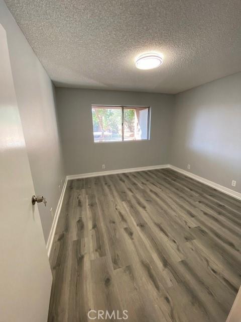 spare room featuring a textured ceiling, dark wood finished floors, and baseboards