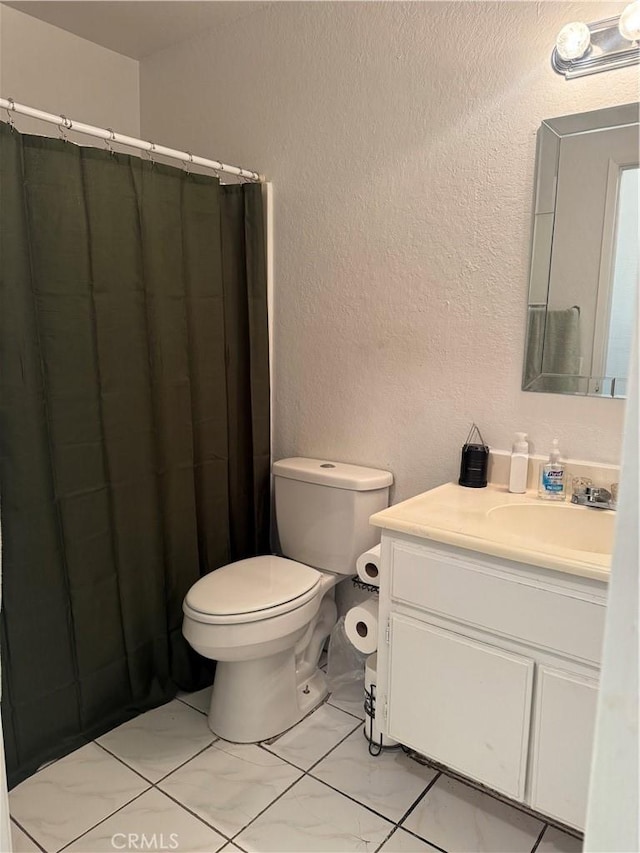 bathroom featuring a textured wall, toilet, a shower with curtain, marble finish floor, and vanity