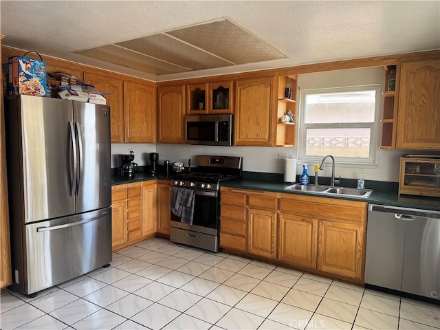 kitchen featuring dark countertops, appliances with stainless steel finishes, brown cabinets, open shelves, and a sink