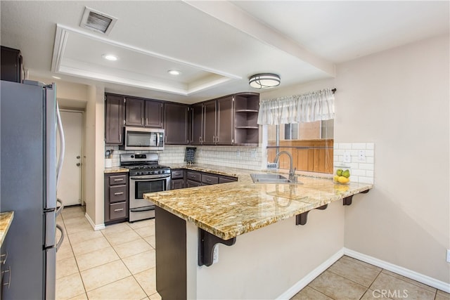 kitchen with a peninsula, appliances with stainless steel finishes, a raised ceiling, and a sink