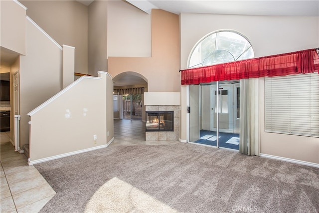 living area with arched walkways, high vaulted ceiling, carpet flooring, tile patterned floors, and a tiled fireplace