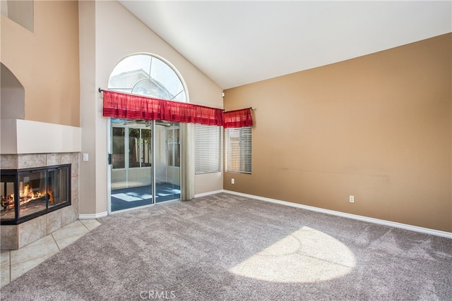 unfurnished living room featuring baseboards, high vaulted ceiling, a tiled fireplace, and light colored carpet