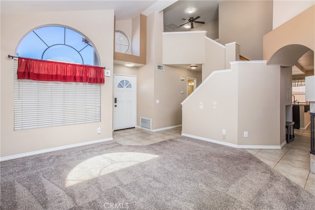 entrance foyer with high vaulted ceiling, light carpet, visible vents, a ceiling fan, and stairway