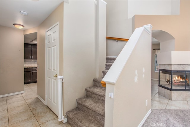 stairway featuring baseboards, a tile fireplace, and tile patterned floors