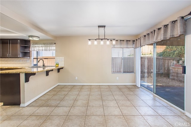 unfurnished dining area featuring a healthy amount of sunlight, a sink, baseboards, and light tile patterned floors