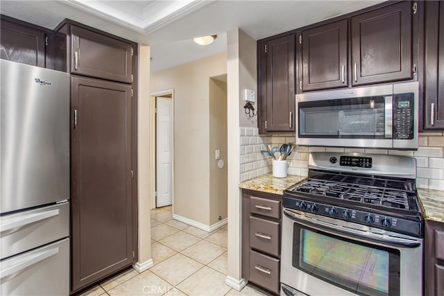 kitchen with light tile patterned floors, light stone counters, dark brown cabinets, appliances with stainless steel finishes, and tasteful backsplash