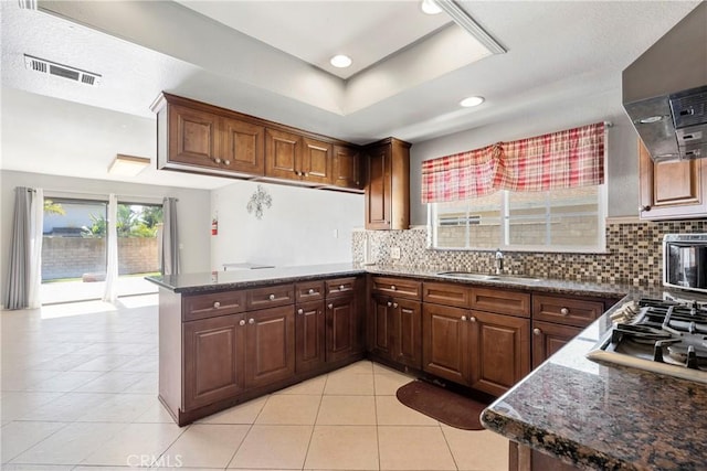 kitchen featuring visible vents, decorative backsplash, a sink, a peninsula, and exhaust hood