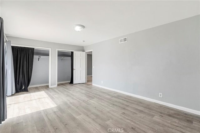 unfurnished bedroom featuring baseboards, two closets, visible vents, and light wood-style floors