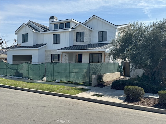 view of front of property featuring a fenced front yard, a chimney, an attached garage, a standing seam roof, and board and batten siding