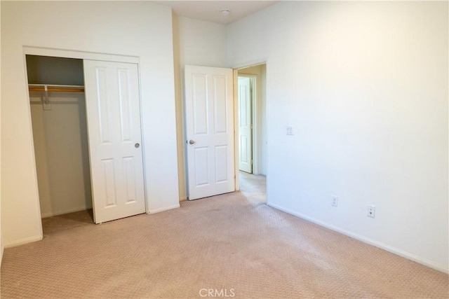 unfurnished bedroom with light carpet, a closet, and baseboards