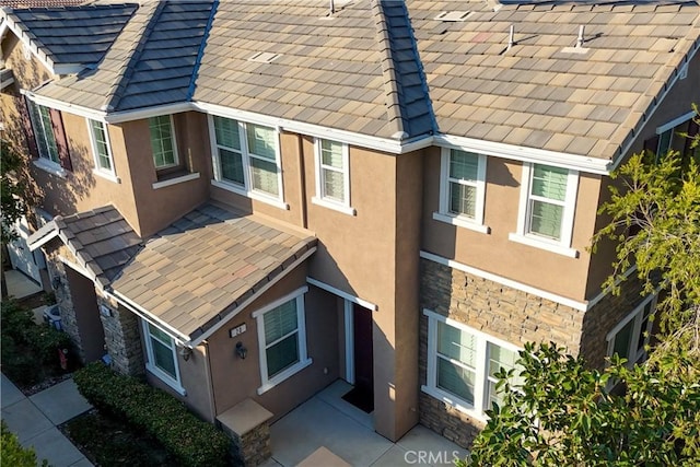 exterior space featuring stone siding, a tile roof, and stucco siding