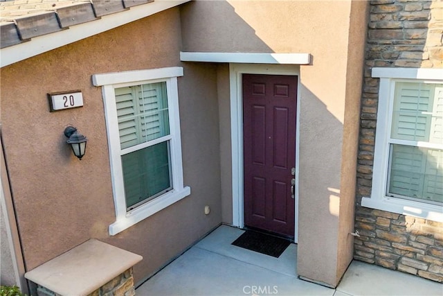 view of exterior entry featuring stone siding and stucco siding