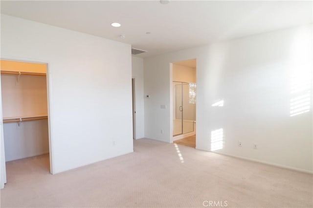 unfurnished bedroom featuring a spacious closet, a closet, visible vents, and light colored carpet