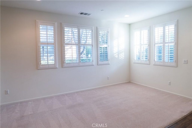 carpeted empty room with a healthy amount of sunlight, visible vents, and baseboards