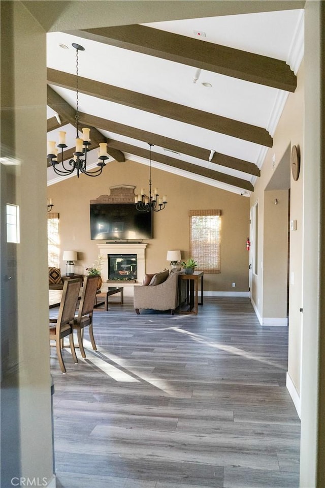 living area with vaulted ceiling with beams, wood finished floors, baseboards, a glass covered fireplace, and an inviting chandelier