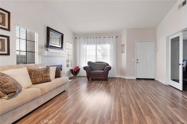 living area with a tile fireplace, a high ceiling, wood finished floors, visible vents, and baseboards