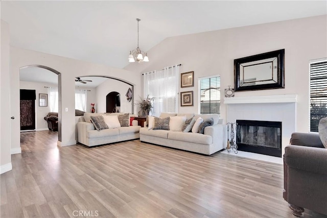 living room with arched walkways, a healthy amount of sunlight, lofted ceiling, and light wood finished floors