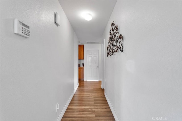 hallway with visible vents, baseboards, and wood finished floors