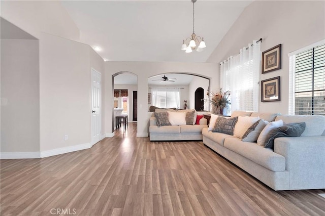 living room featuring arched walkways, a notable chandelier, light wood-style flooring, high vaulted ceiling, and baseboards