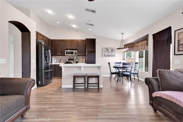 kitchen with dark brown cabinetry, stainless steel appliances, visible vents, open floor plan, and light countertops