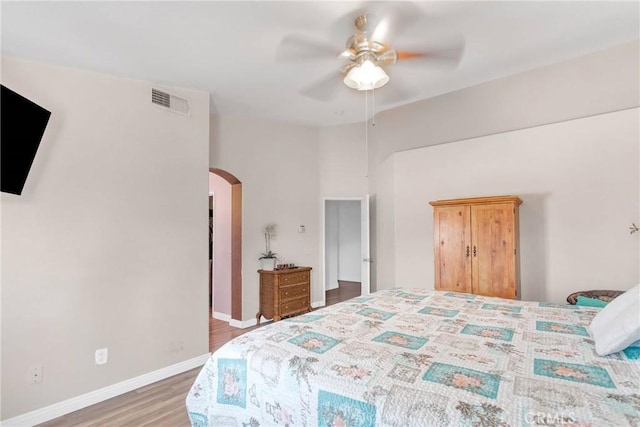 bedroom with baseboards, visible vents, a ceiling fan, arched walkways, and wood finished floors