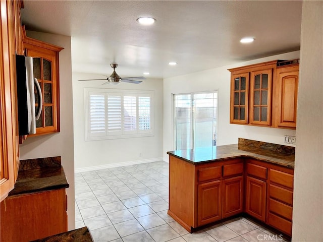 kitchen with brown cabinetry, dark countertops, and glass insert cabinets