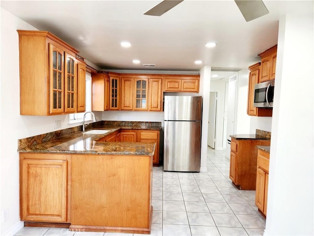 kitchen with appliances with stainless steel finishes, brown cabinetry, glass insert cabinets, a sink, and a peninsula