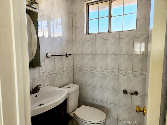 half bath with toilet, tile walls, and a sink