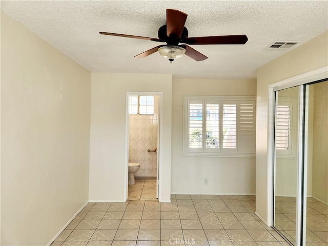 unfurnished bedroom with a textured ceiling, light tile patterned flooring, visible vents, a closet, and ensuite bath