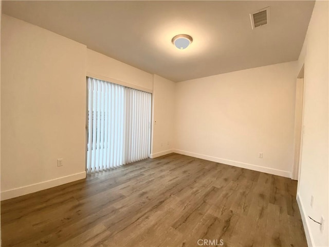 spare room with dark wood-style floors, visible vents, and baseboards