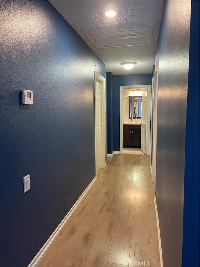 hall with attic access, baseboards, a textured ceiling, and light wood finished floors