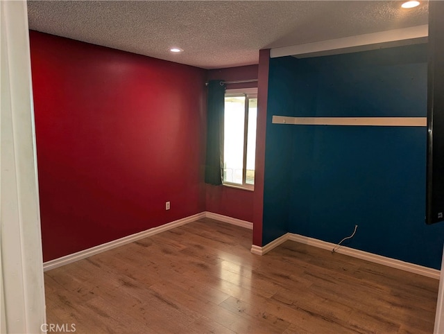 empty room with recessed lighting, a textured ceiling, baseboards, and wood finished floors