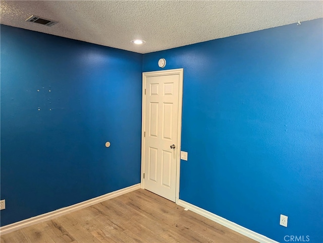 unfurnished room with visible vents, a textured ceiling, baseboards, and wood finished floors