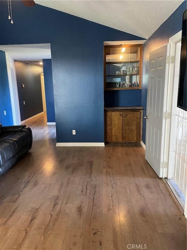 bar featuring vaulted ceiling, a textured ceiling, baseboards, and wood finished floors