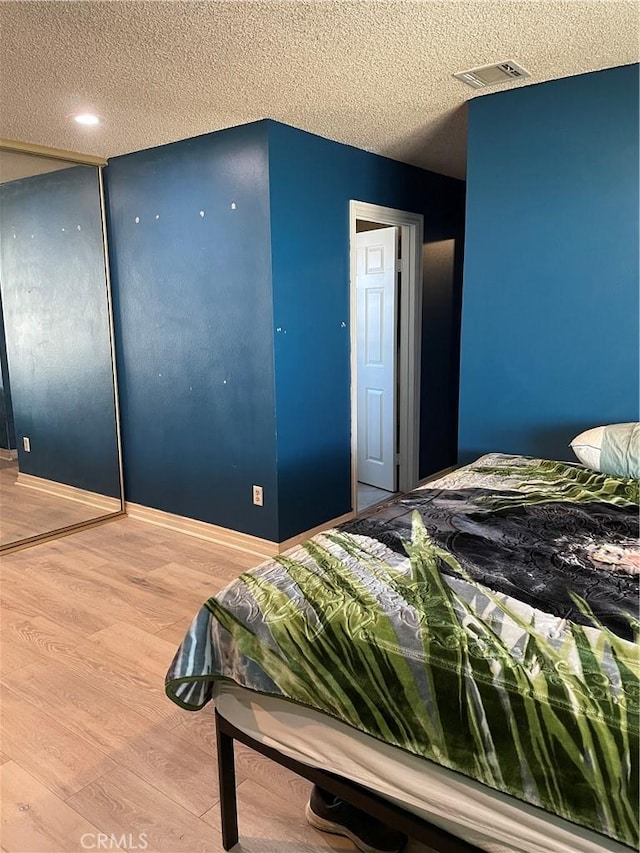 bedroom with a textured ceiling, a closet, wood finished floors, and visible vents