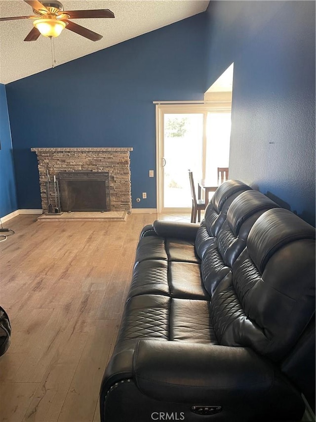 living area featuring lofted ceiling, ceiling fan, wood finished floors, a textured ceiling, and a stone fireplace