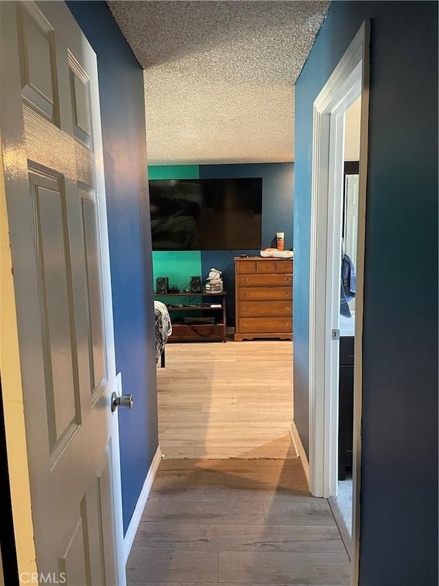 hallway with a textured ceiling, baseboards, and wood finished floors